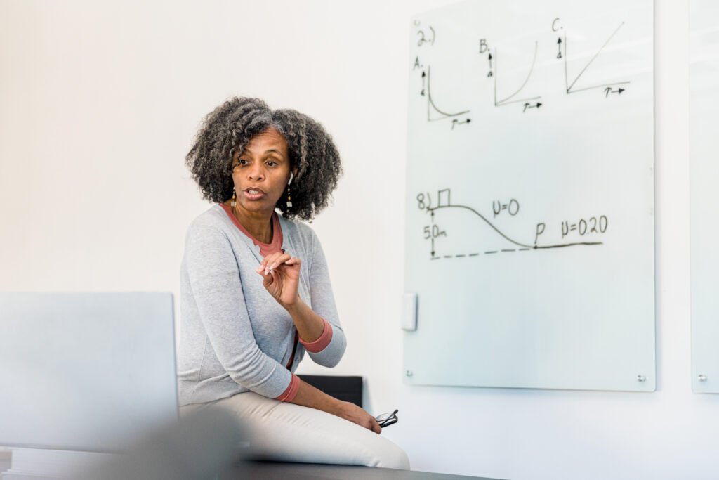 Professora de física ensinando princípios da disciplina na sala de aula perto de um quadro com gráficos