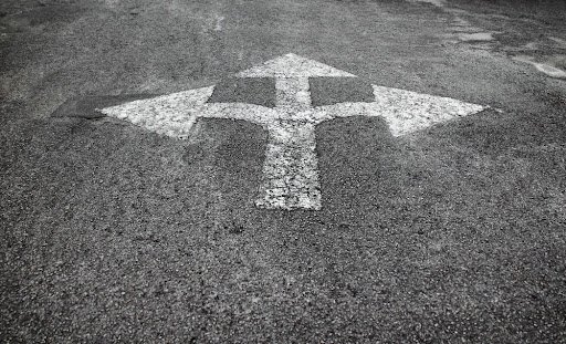 A three way arrow symbol on a black asphalt road surface. 
