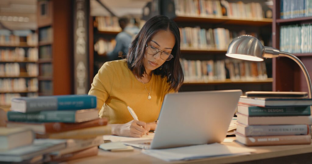 mulher estudando com uma pilha de livros e o notebook aberto 