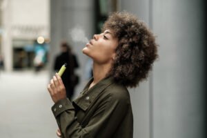 Mulher de cabelos cacheados assoprando fumaça e com um cigarro eletrônico amarelo na mão esquerda