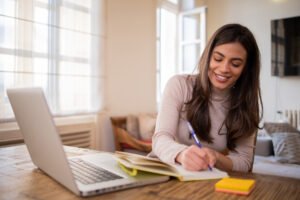 Mulher jovem estudando em casa com um caderno e um computador